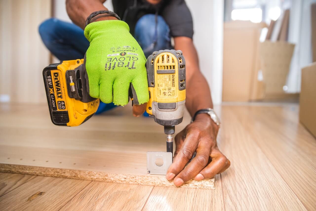 Person crouched down on the floor using a Dewalt driver to screw in hardware to a piece of wood