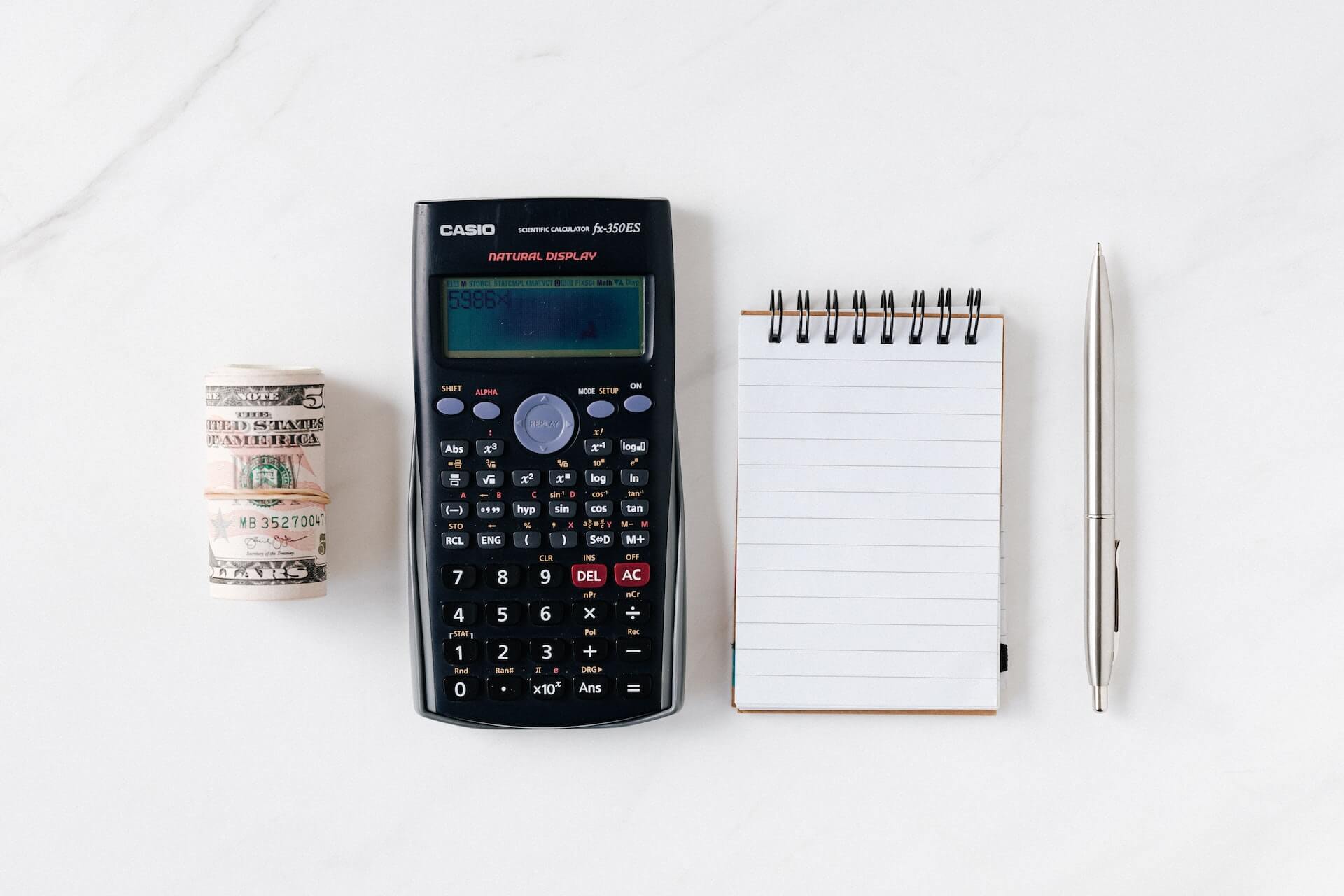 Role of USD, a Casio calculator, a small note pad, and a pen