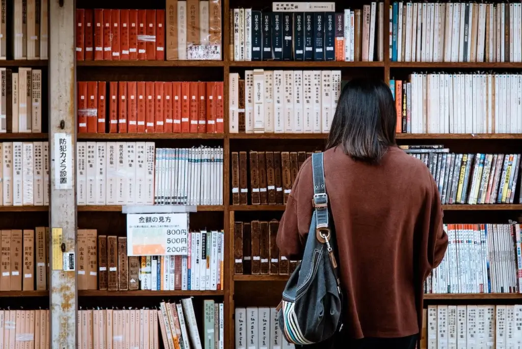 University student with back to camera standing in front of books at the library